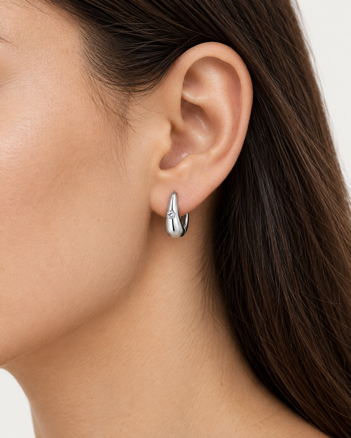 Silver Audrey teardrop moissanite huggie earring worn on an adult ear to show scale