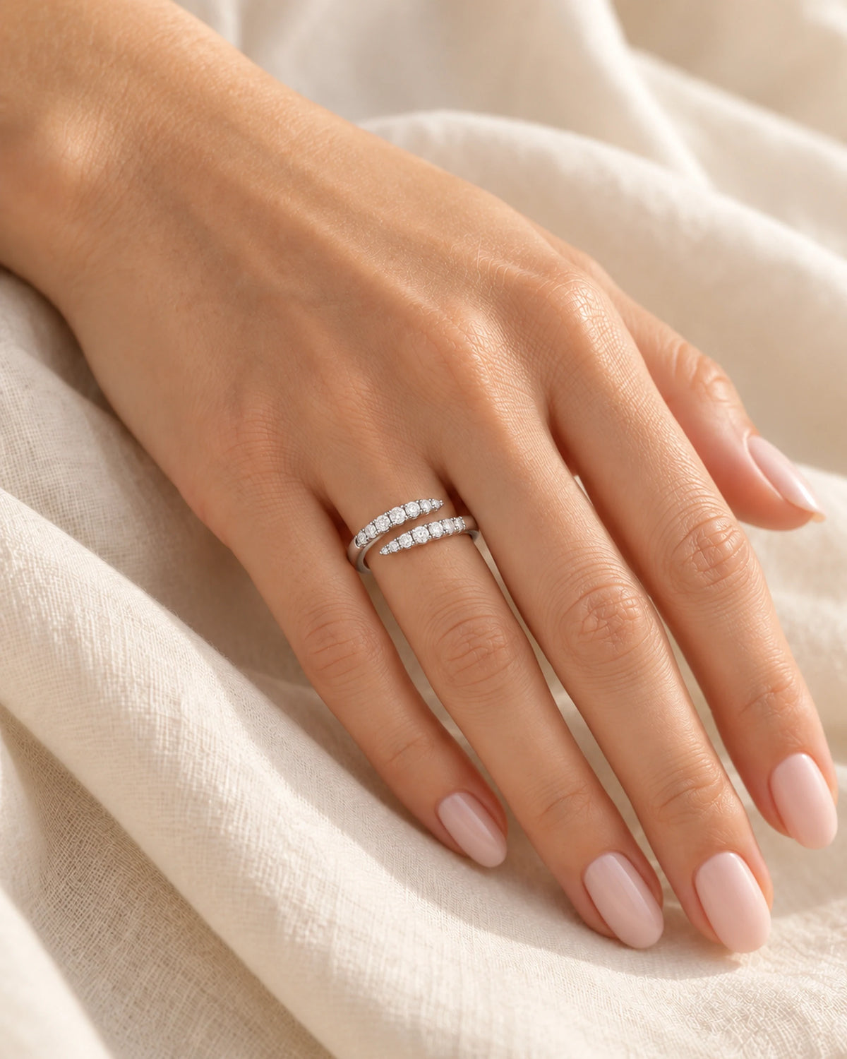 Clara silver open-wrap moissanite ring worn on a hand resting on cream fabric, showing the fit and open-front design.
