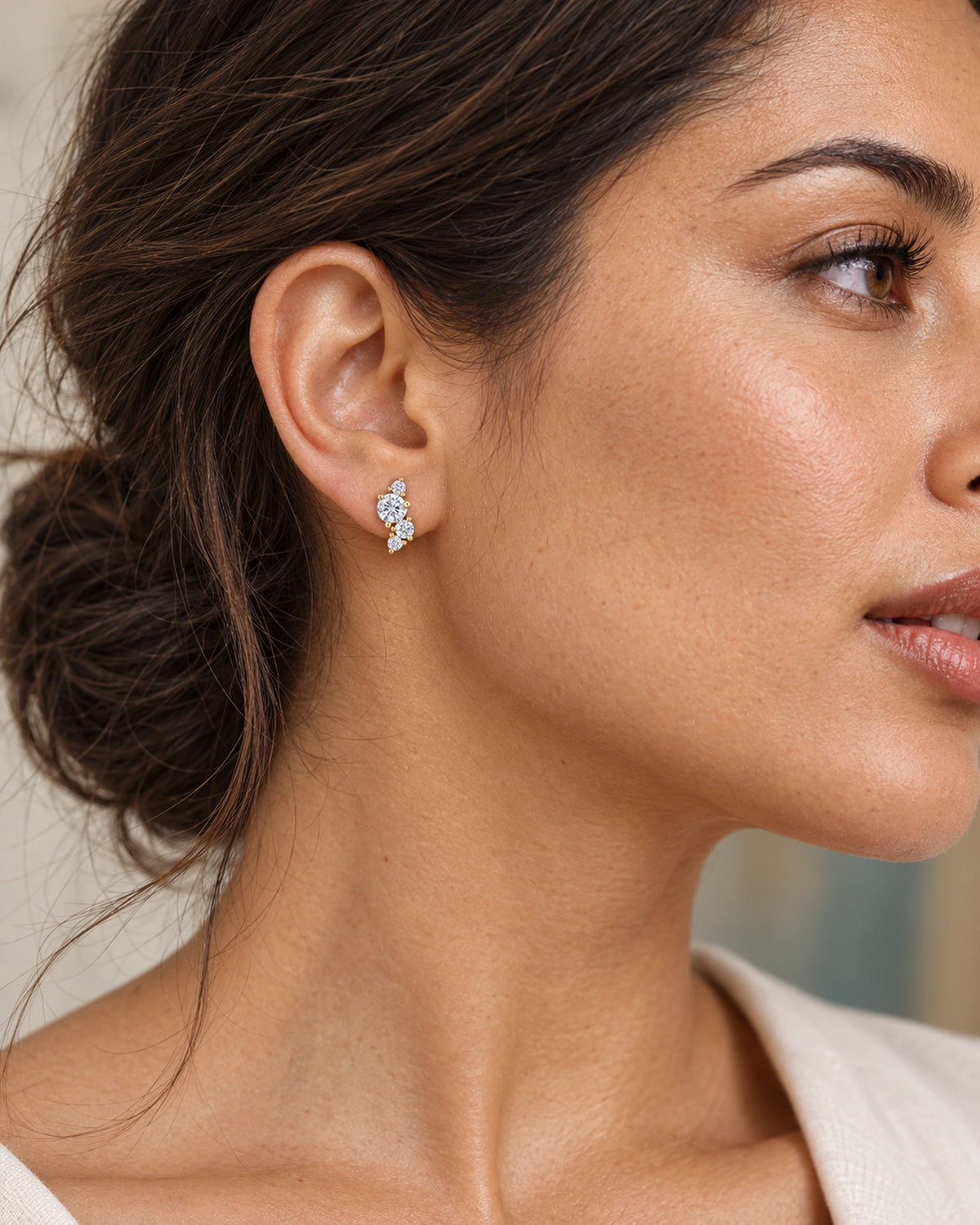 Juliette gold-tone cluster stud worn on an adult model with swept-back brown hair, showing four graduated round moissanite stones in an asymmetric setting.